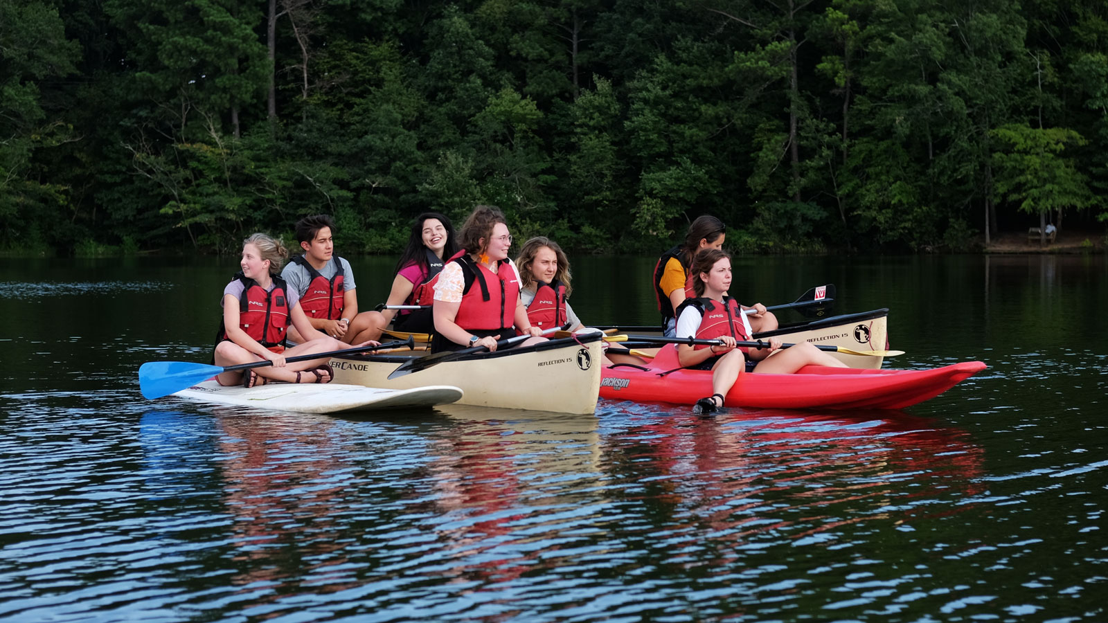 A group of students relax in canoes and kayaks on a lake.